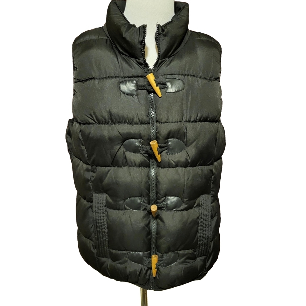 Large black puffer vest featuring a high collar,zipper,wooden toggle closure.